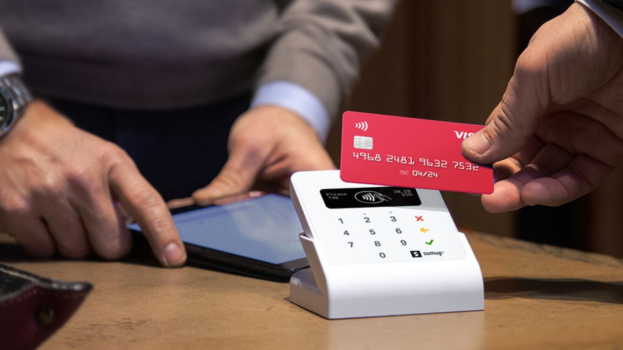 A person holds a tablet linked to a payment card reader and another person holds a credit card