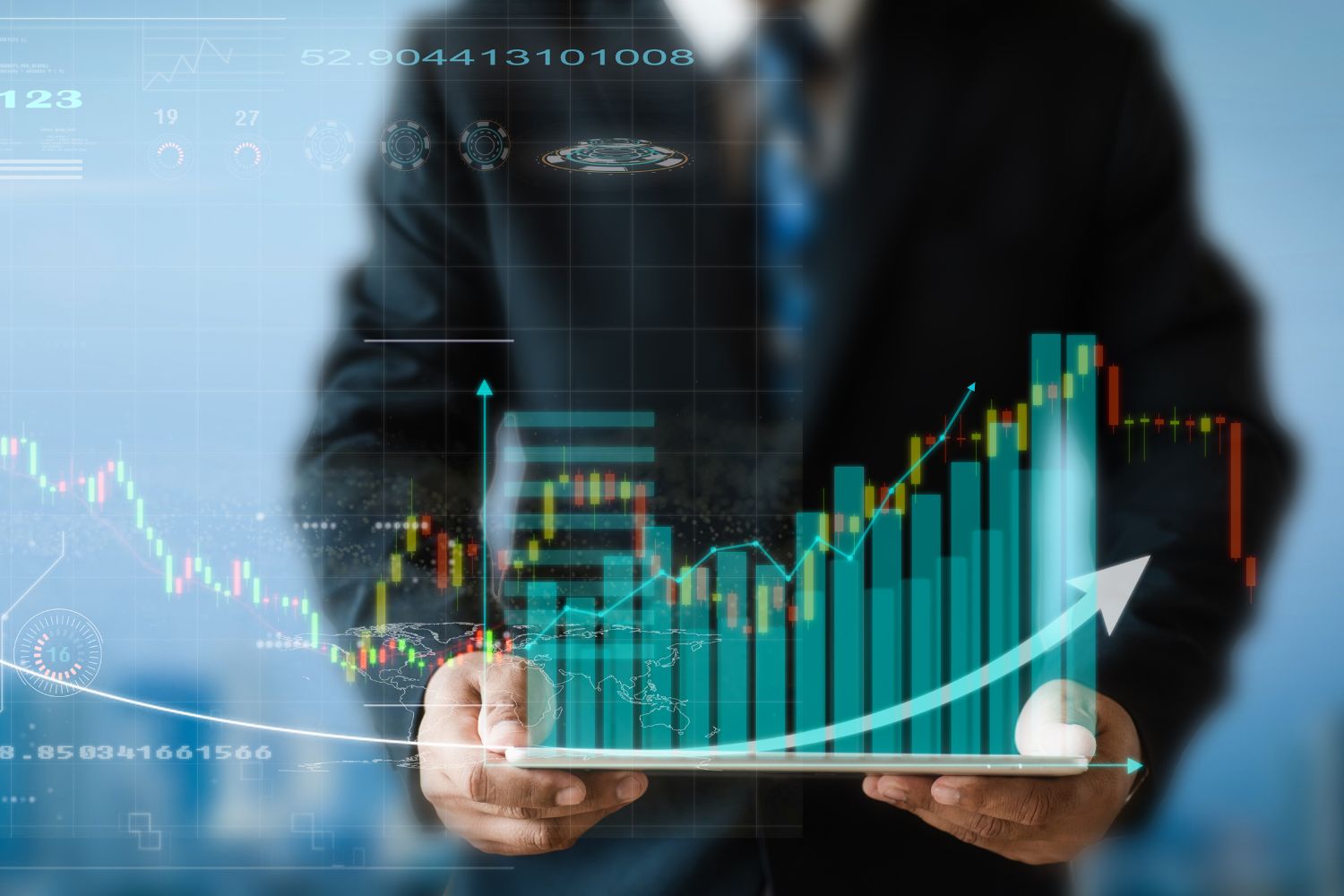 A man in a suit is holding a tablet with a futuristic display of economic charts displayed above.