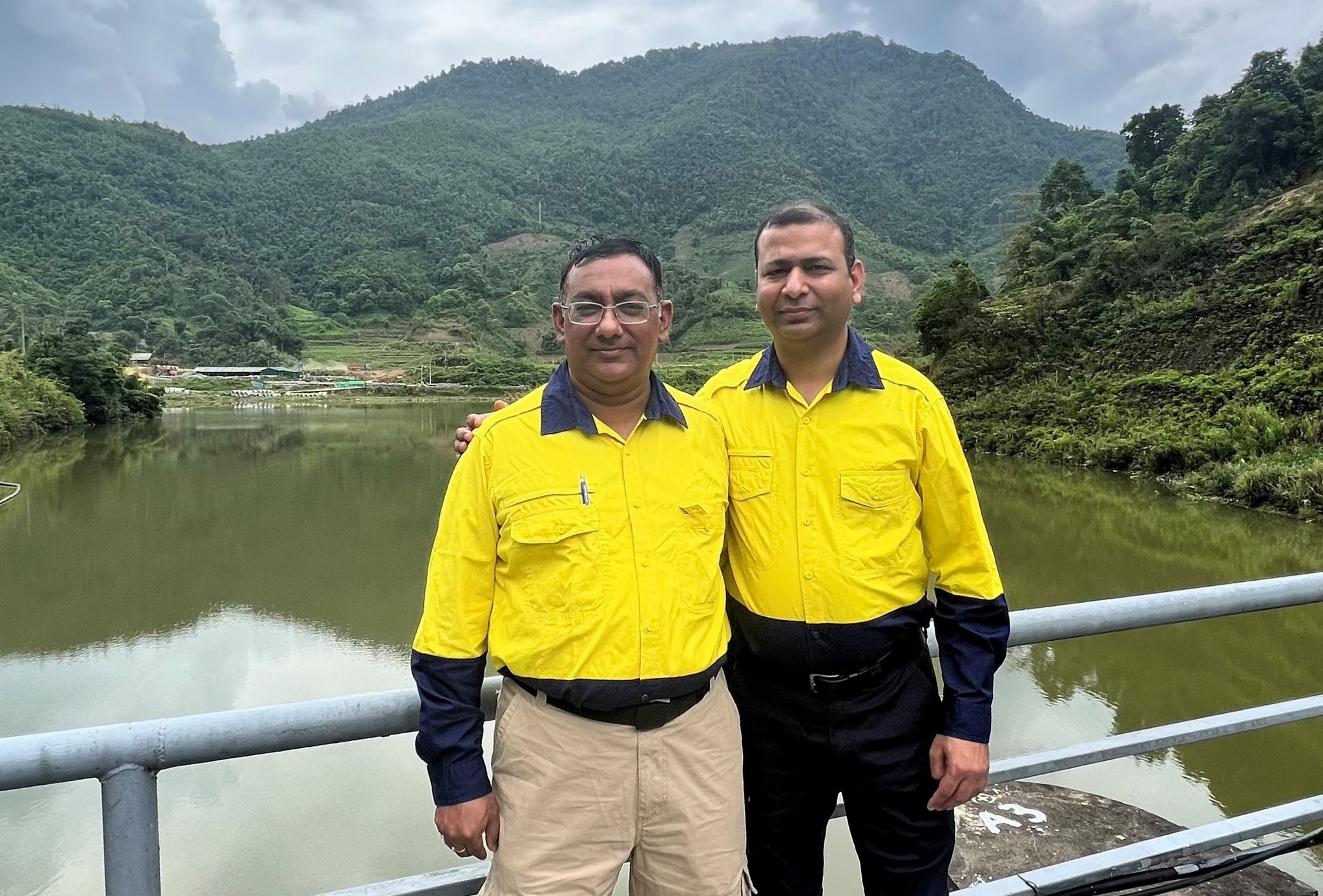 Two men standing on a dam with a mountain in the background