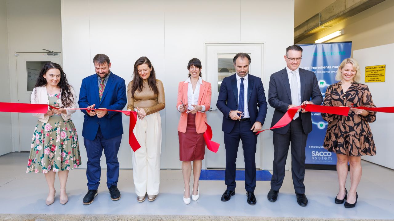 A group of seven people cutting a ribbon at the opening of Sacco System's Brisbane development facility.