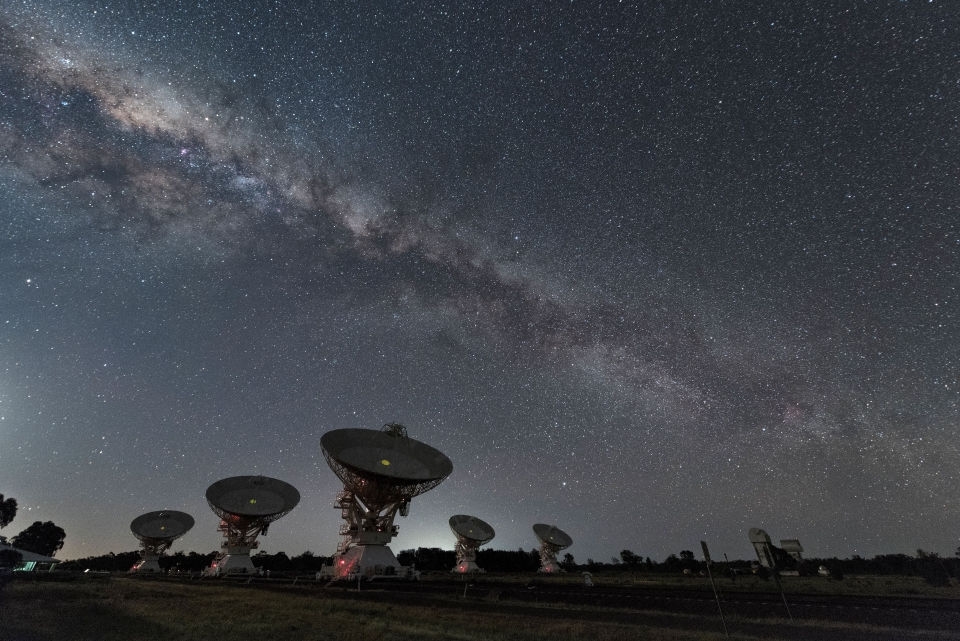 View of the night sky over large satellite dishes.