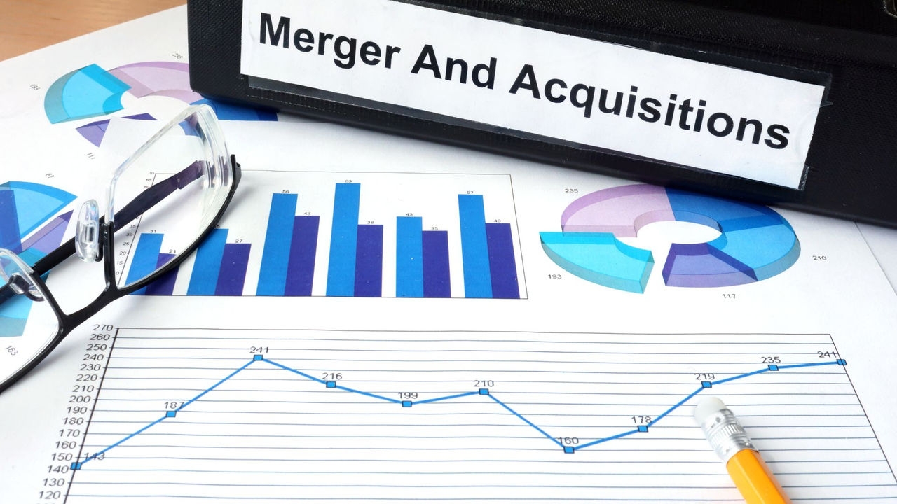 A pair of glasses are set down on a chart printout and a folder titled mergers and acquisitions.