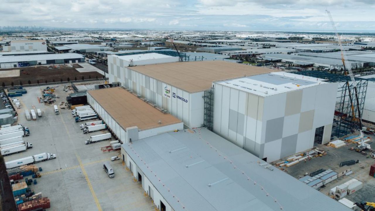 A group of metal clad factory buildings housing a cold storage facility with the Melbourne city skyline in the distant background