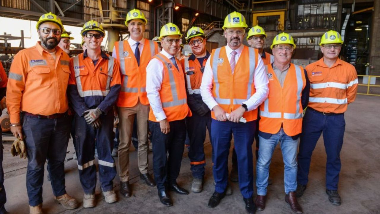 Picture of a group of steel workers wearing orange safety vests and yellow hard hats