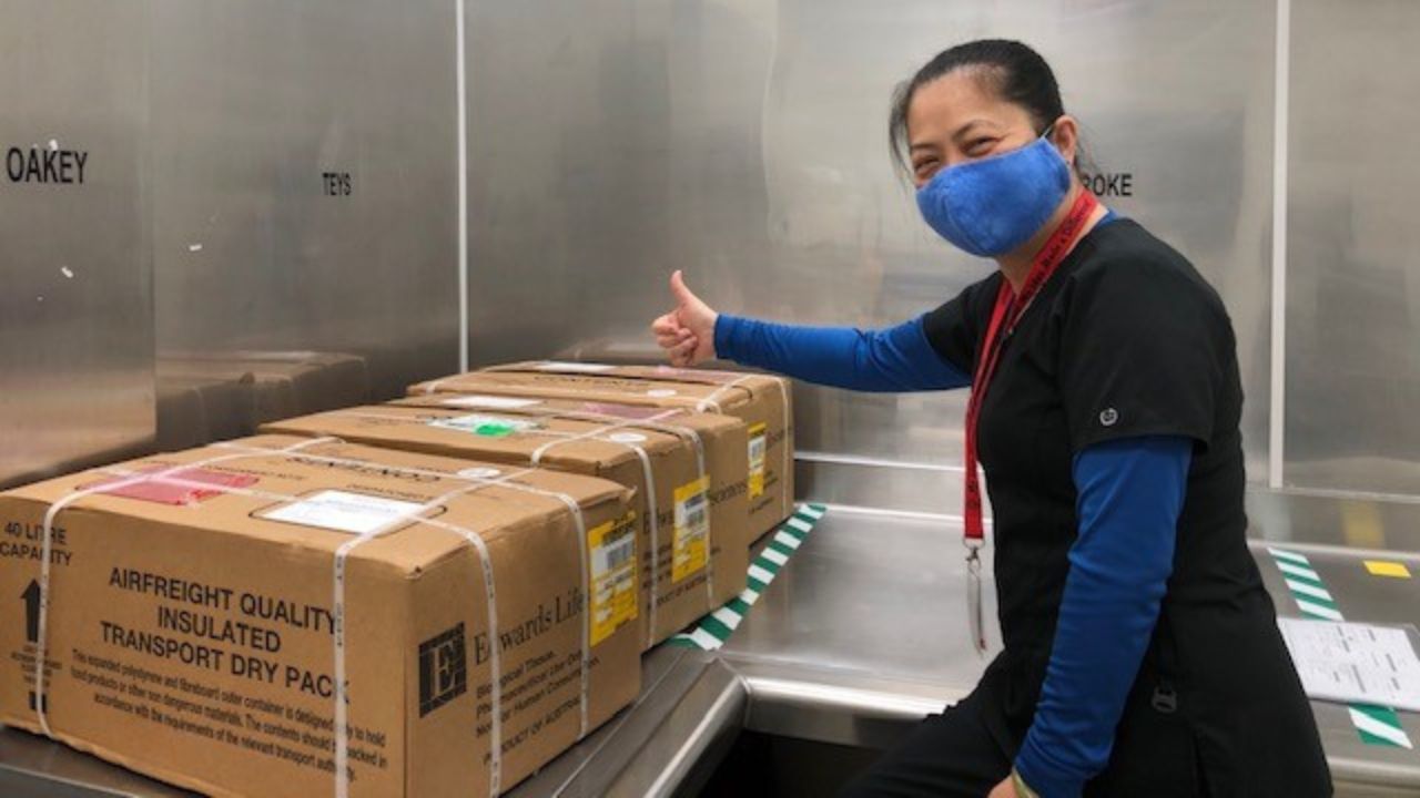 A woman in a surgical mask and scrubs giving a thumbs-up for three boxes containing Australian bovine tissue
