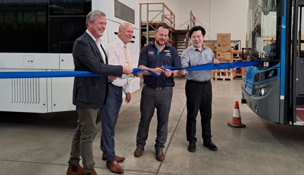 4 men in a warehouse cutting a ribbon in front of an electric bus