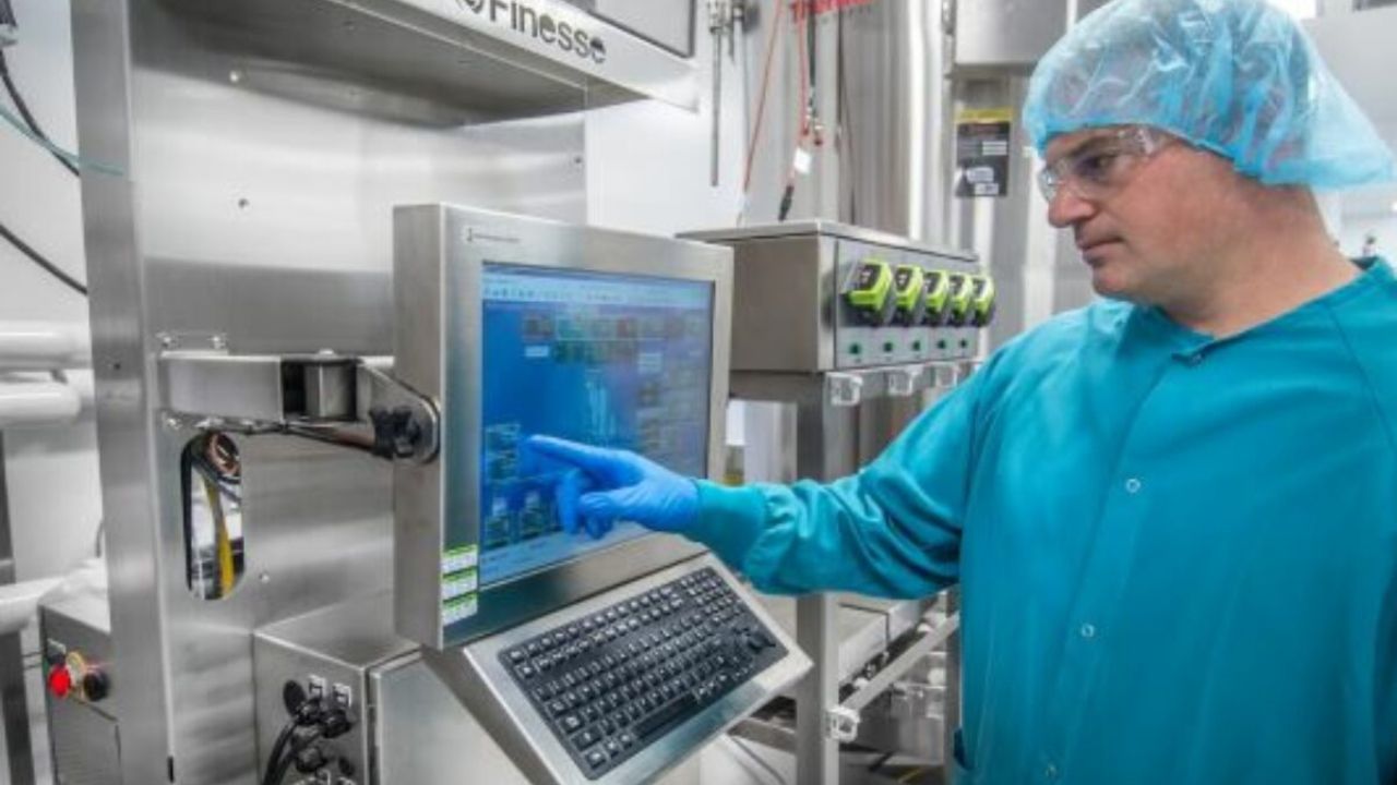 A male technician wearing a blue lab coat, hair net and safety glasses, inputs commands via a screen during the vaccine manufacturing process. Credit: www.aumanufacturing.com.au