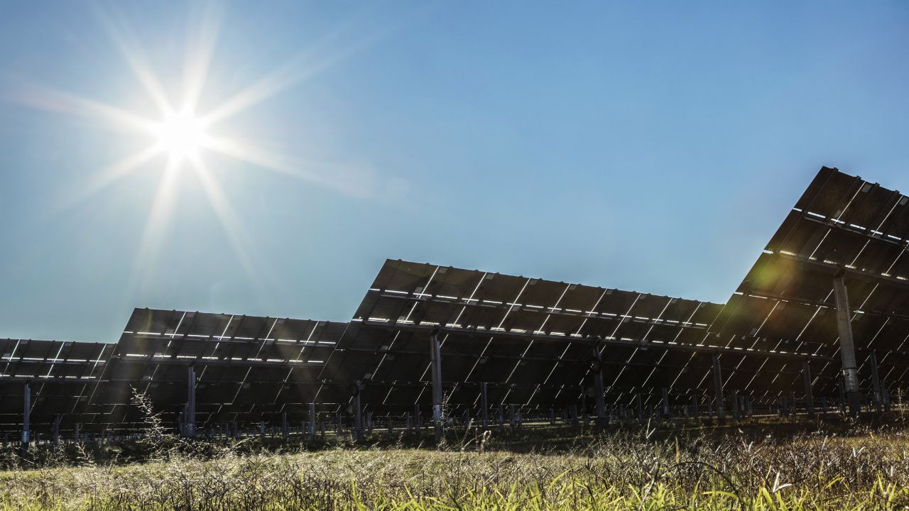 Solar panels in a grass field with a bright sun in a blue sky